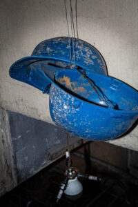 Blue hard hat helmets, strung together with copper with a spark plugs and a light bulb below